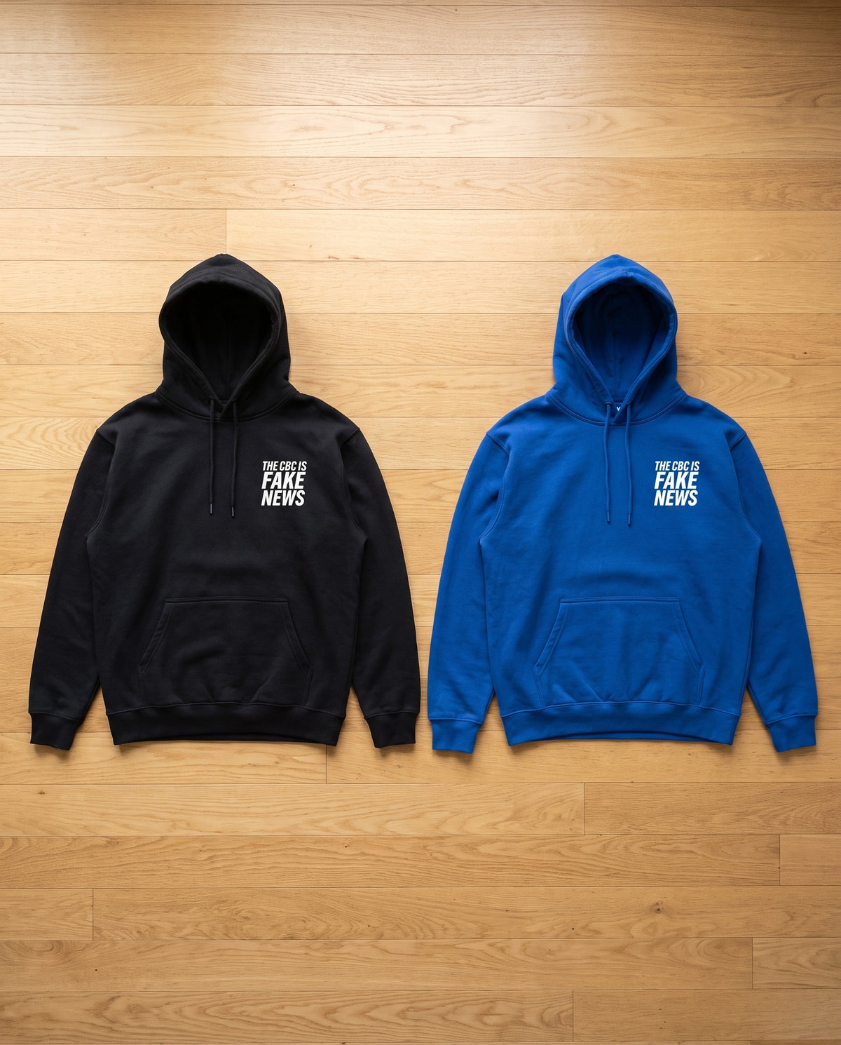 The CBC Is FAKE NEWS hoodie flat lay, black and royal blue side by side, fronts showing the small chest print
