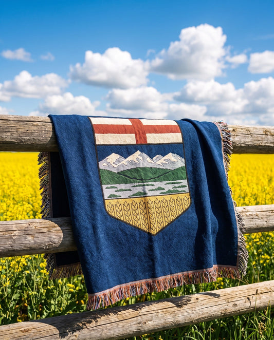 Alberta Flag Woven Blanket draped over a fence rail in a canola field under blue sky