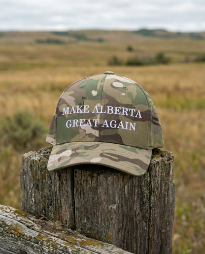 Camouflage cap with 'MAKE ALBERTA GREAT AGAIN'  Hat text on a wooden post in a field.