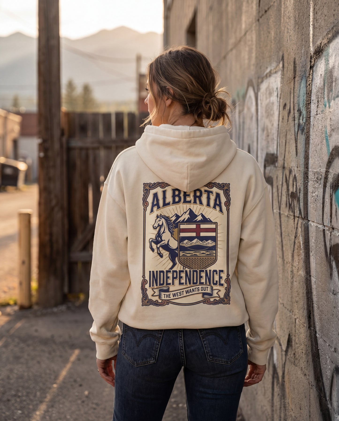 Person wearing a hoodie with 'Alberta Independence' design, standing against a graffiti-covered wall.