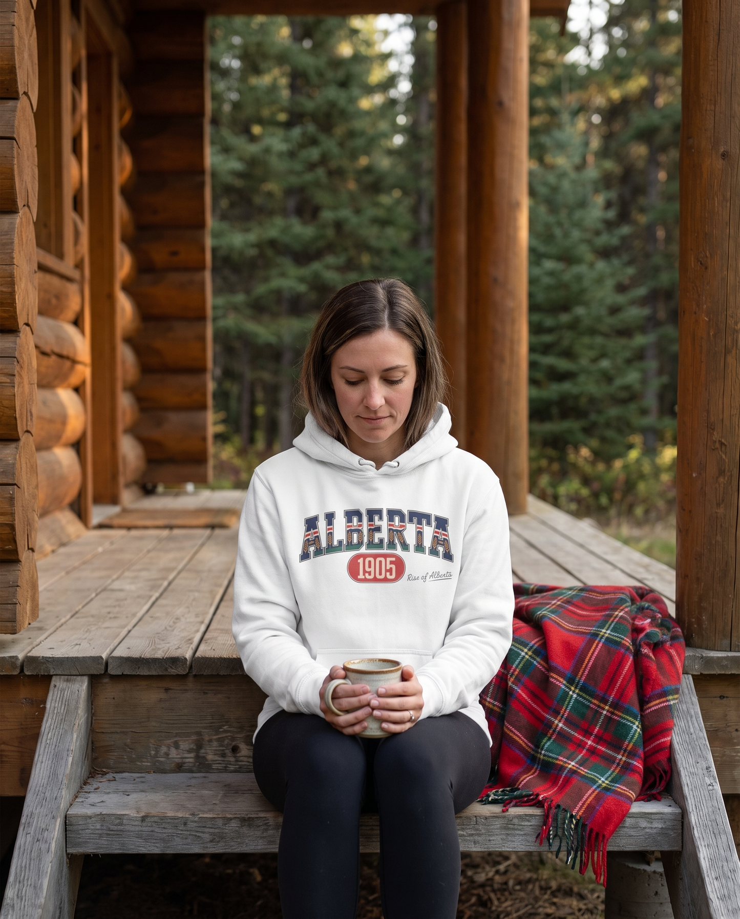 Woman wearing white Alberta 1905 hoodie with coffee on cabin porch