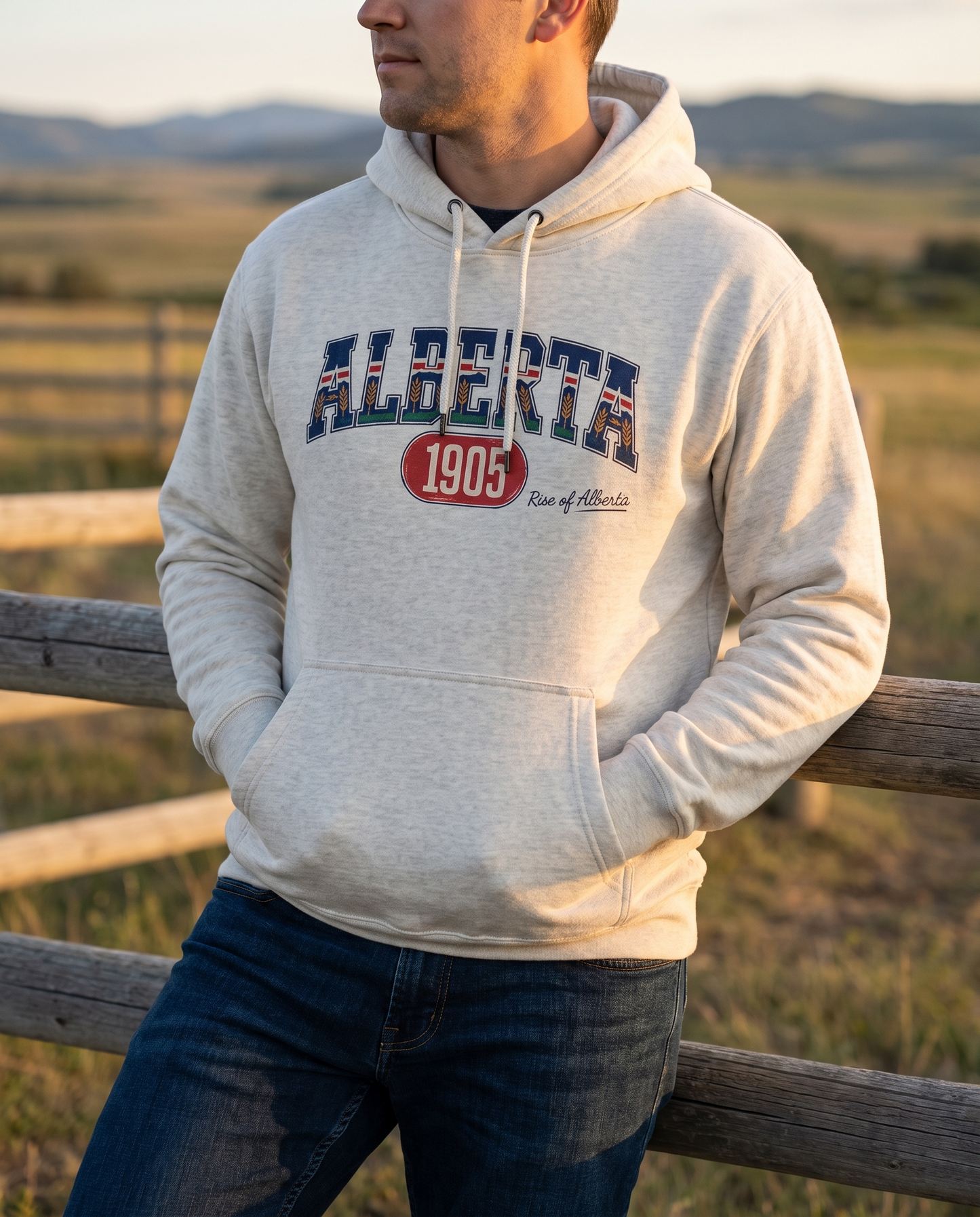 Man wearing oatmeal heather Alberta 1905 hoodie at ranch fence golden hour