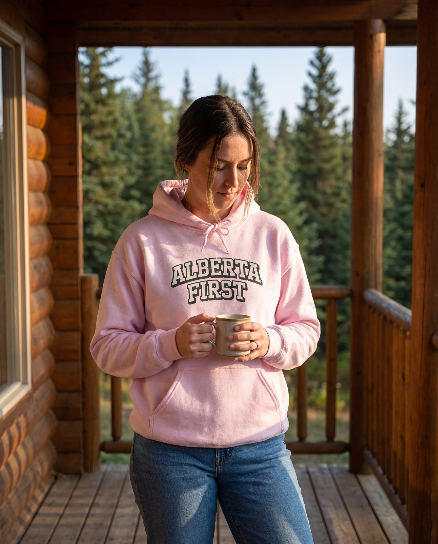 Woman wearing light pink Alberta First varsity hoodie on cabin porch