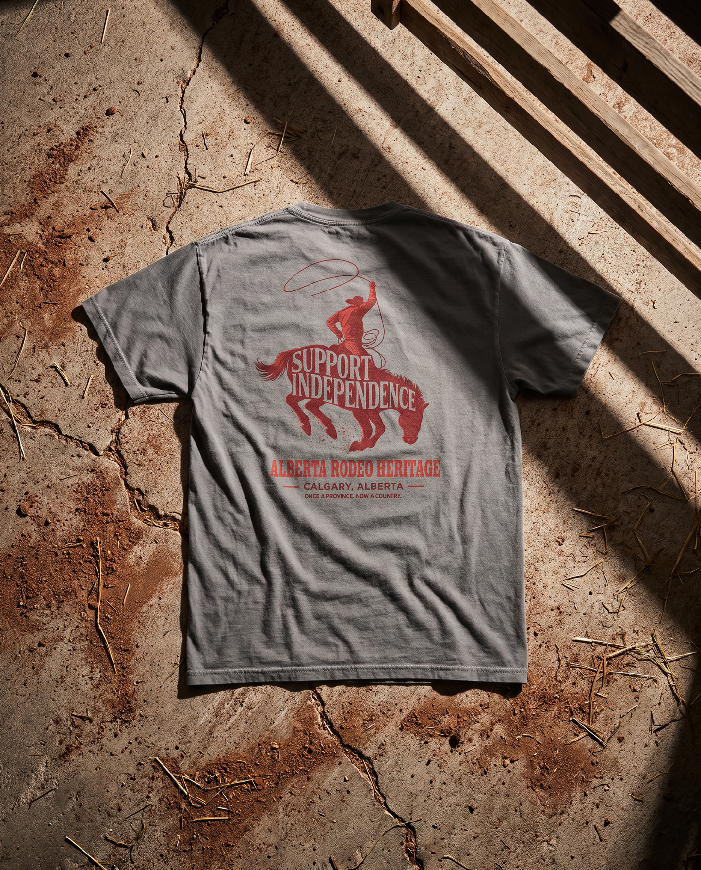 Stampede Rider Free Alberta tee granite back print on cracked concrete with gate shadows