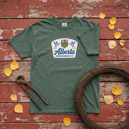 Alberta Independence Co. Heritage Tee in Blue Spruce, flat lay on barn red boards