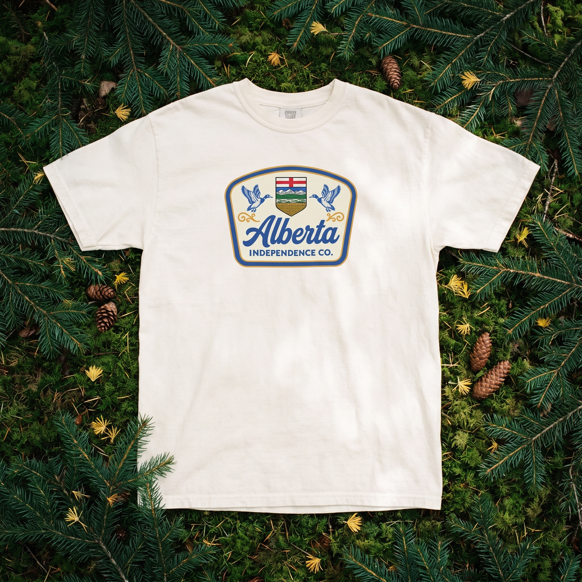 Heritage Tee in Ivory, flat lay on spruce boughs