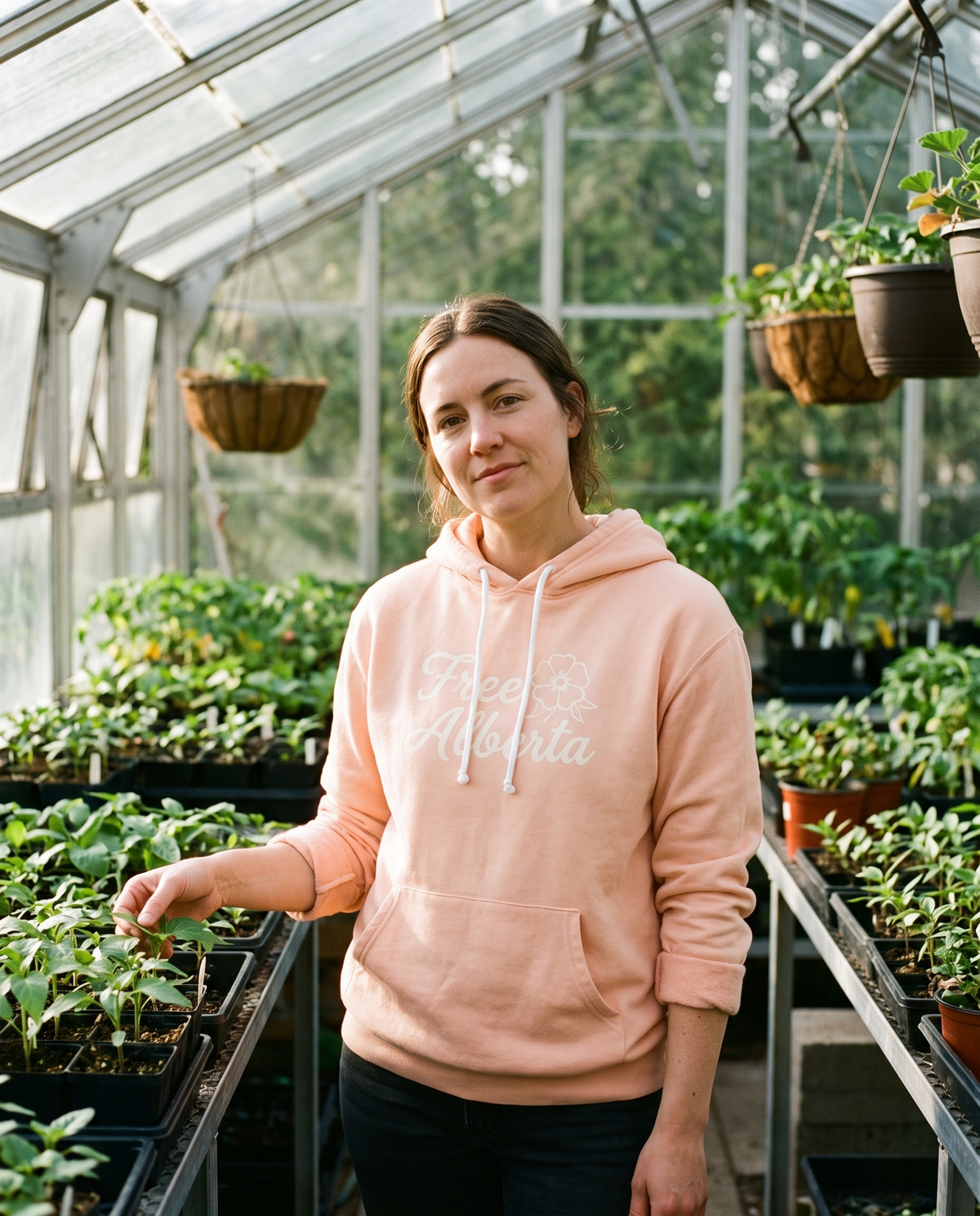 Woman wearing the Peachy Free Alberta hoodie in a greenhouse